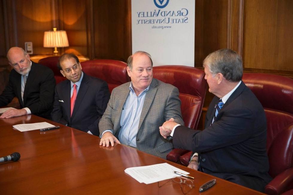 three men at table, two shaking hands